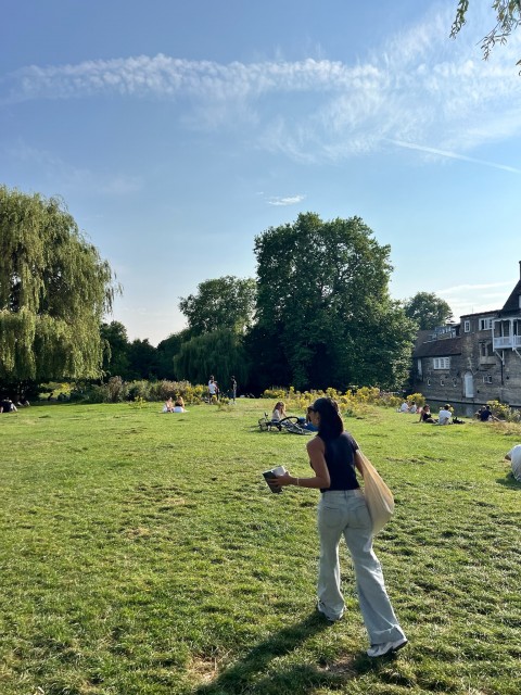 Chabelly Acosta walking through a green park with a cup of coffee in their hand