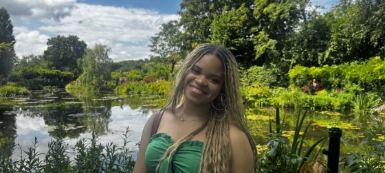 Brooklynne smiling and standing in front of a green garden