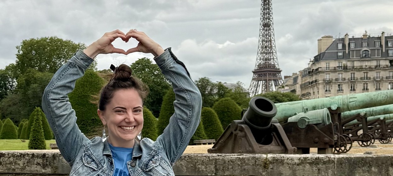 Ashlynn holding her hands up in the shape of a heart with the Effiel Tower in the background