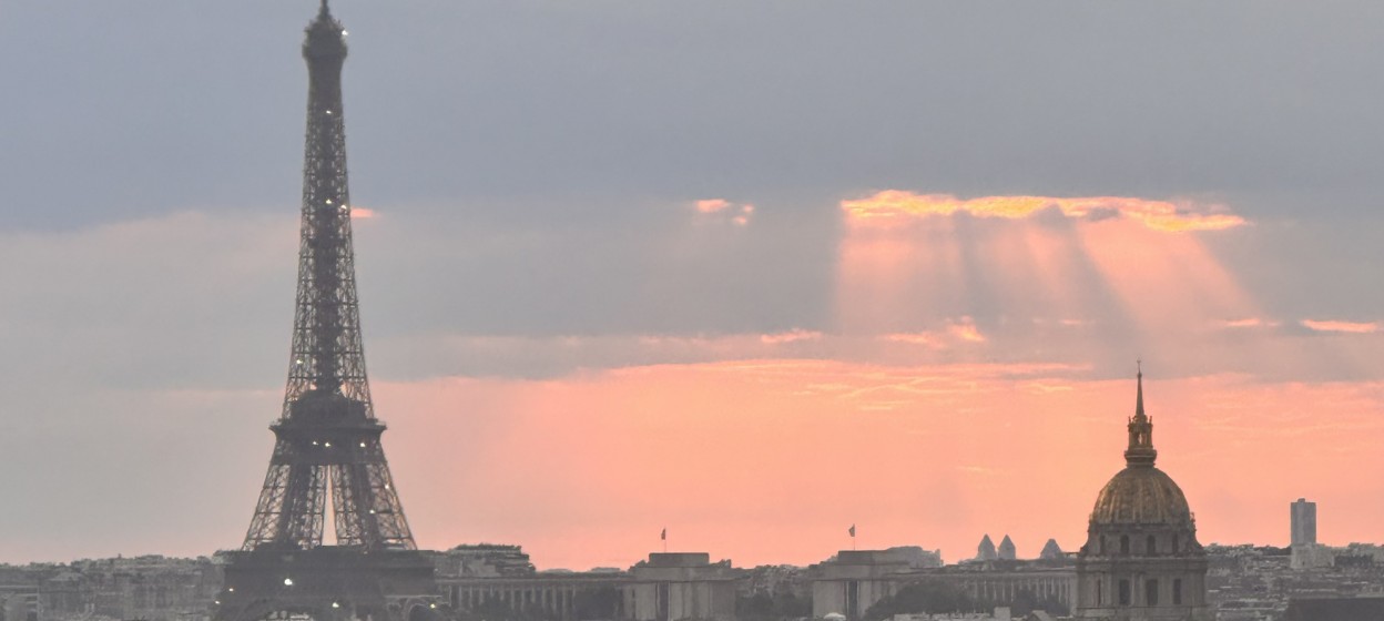 Skyline of Paris with the view of the Effiel Tower and a ray of organe/pink sun shining through dark clouds