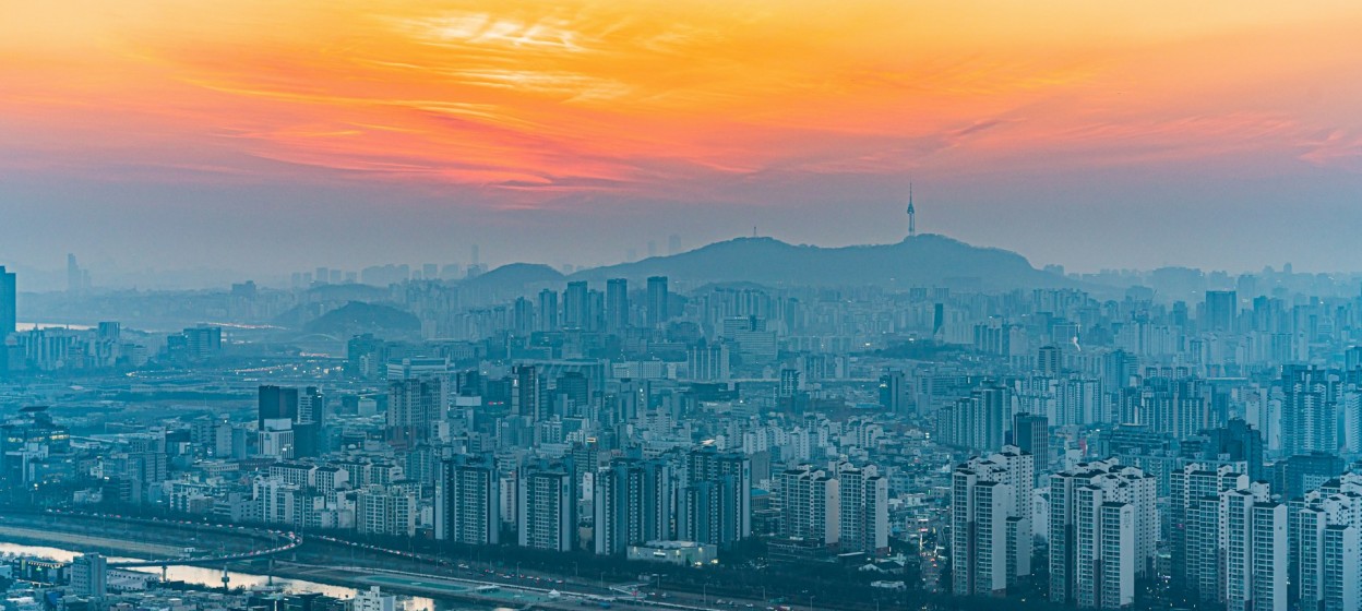 A view of Seoul's buildings with a bright orange sunset in the background