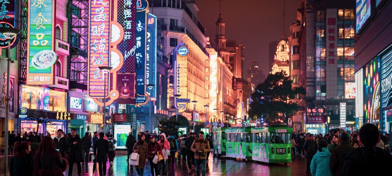 People walking a street at night in Shanghai, China. Brightly colored neon signs light the city street.