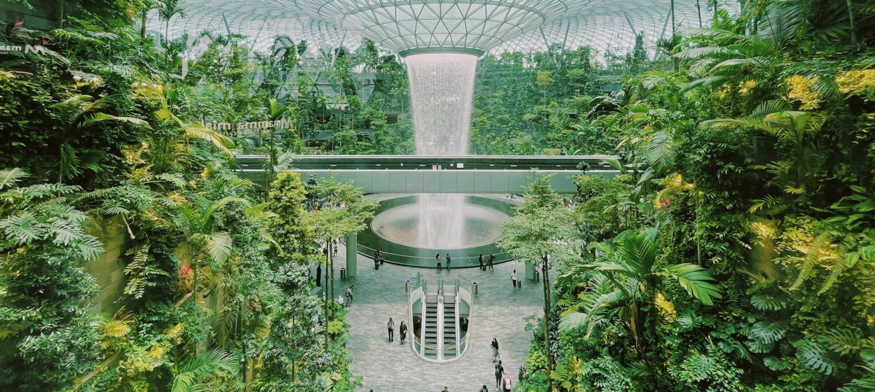 A view of the inside of a building full of greenery and a large water fountain