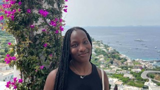 Amara Onyeukwu standing in front of a pretty bunch of flowers and overlooking the sea in Italy