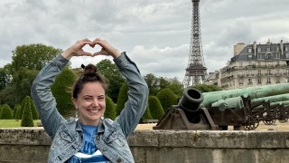 Ashlynn holding her hands up in the shape of a heart with the Effiel Tower in the background
