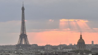 Skyline of Paris with the view of the Effiel Tower and a ray of organe/pink sun shining through dark clouds