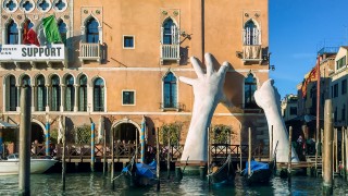 Sculpture of hands supporting a building on the grand canal in Venice, Italy