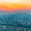 A view of Seoul's buildings with a bright orange sunset in the background
