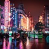 People walking a street at night in Shanghai, China. Brightly colored neon signs light the city street.